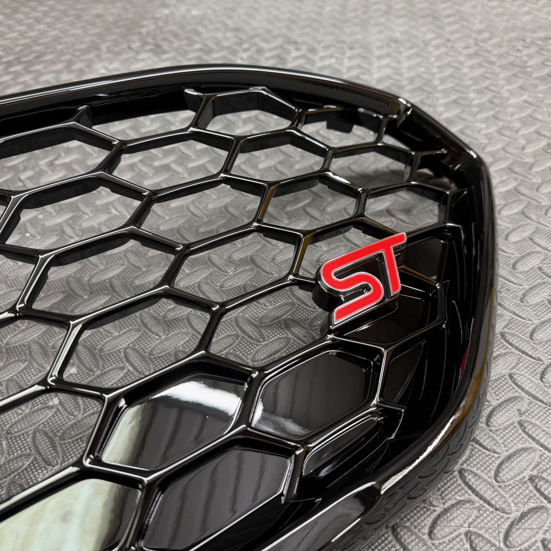 Close-up of a car grille with a red 'ST' logo on a textured gray background