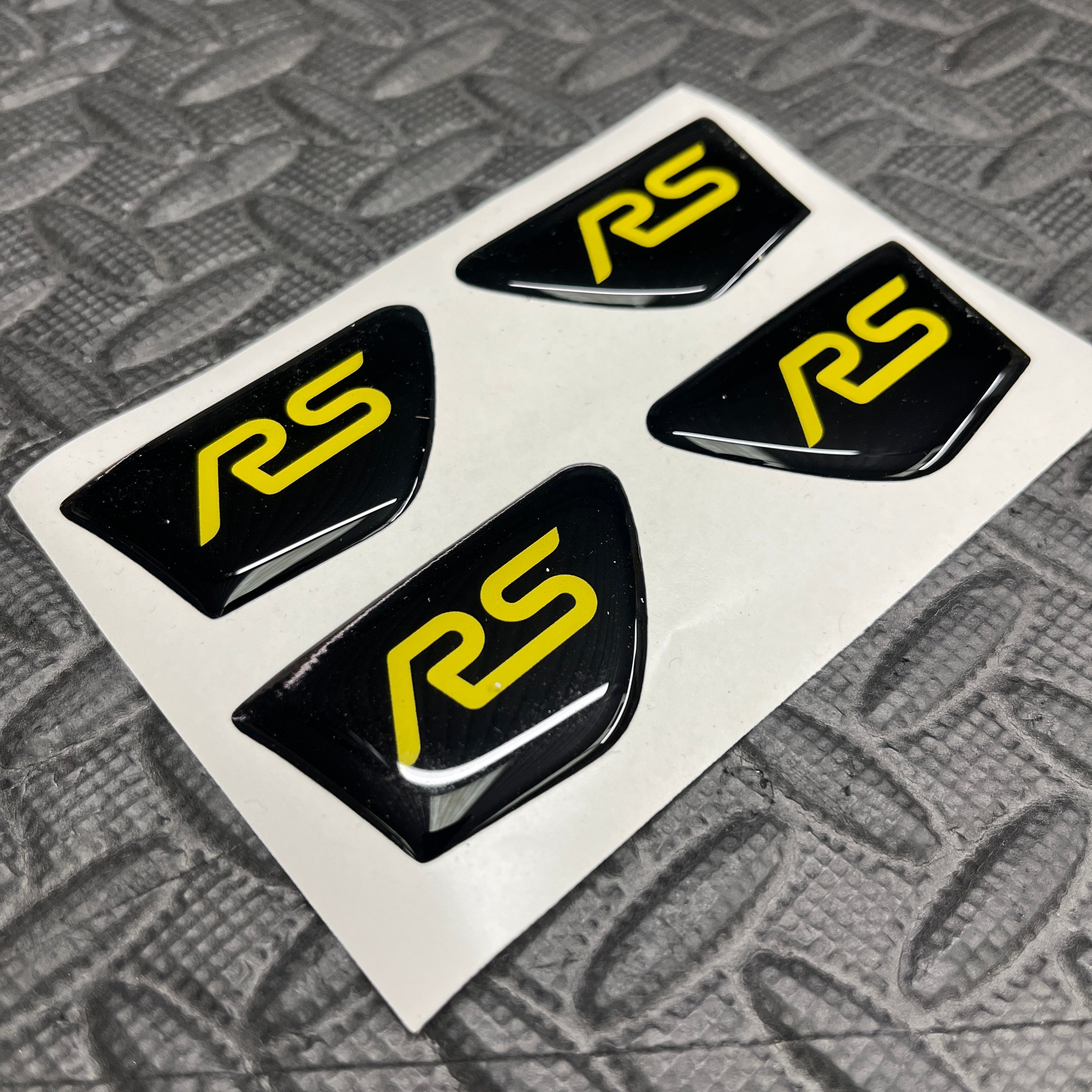 Four black and yellow 'RS' logos on a white card with a textured gray background.
