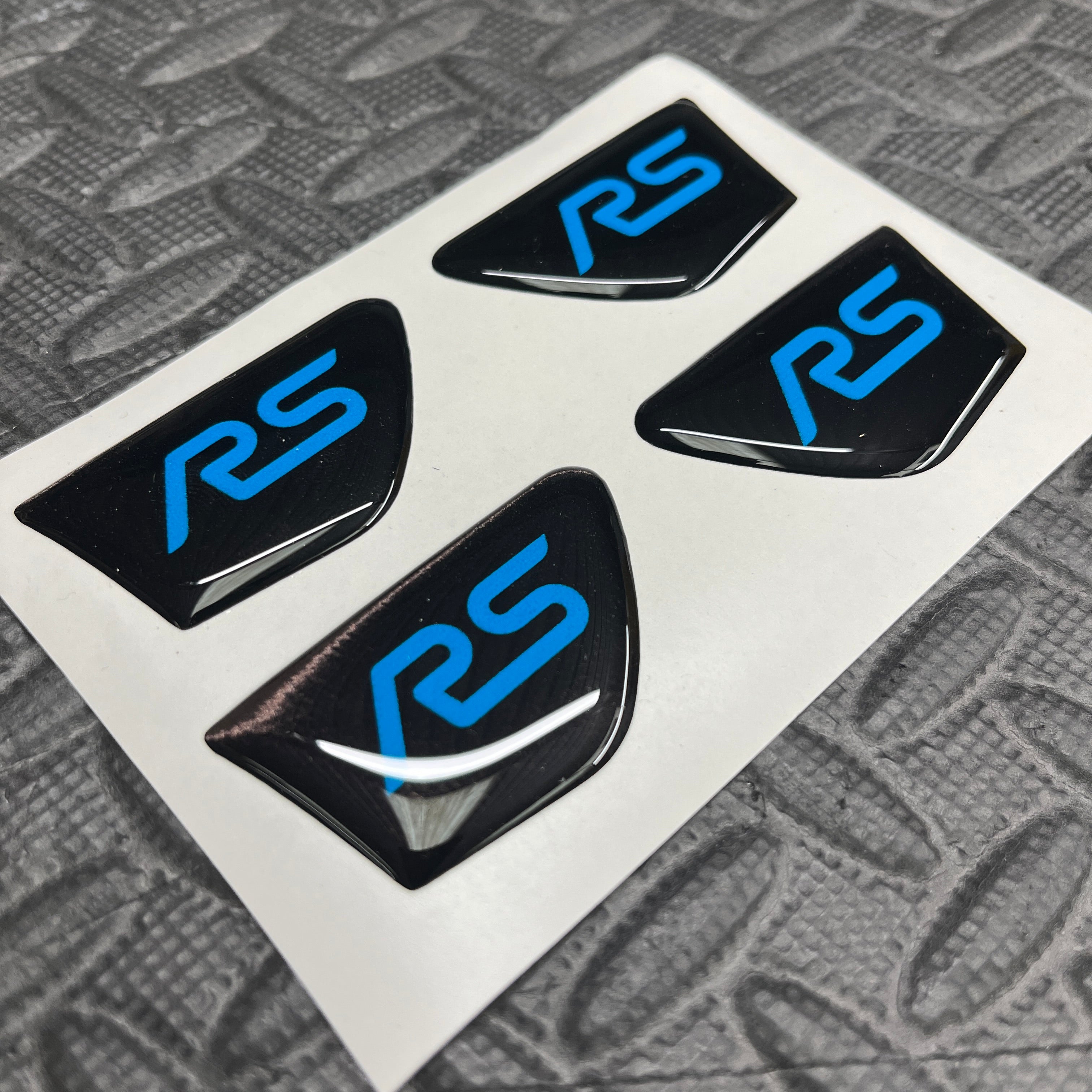 Four black and blue 'RS' logos on a white card with a textured gray background.