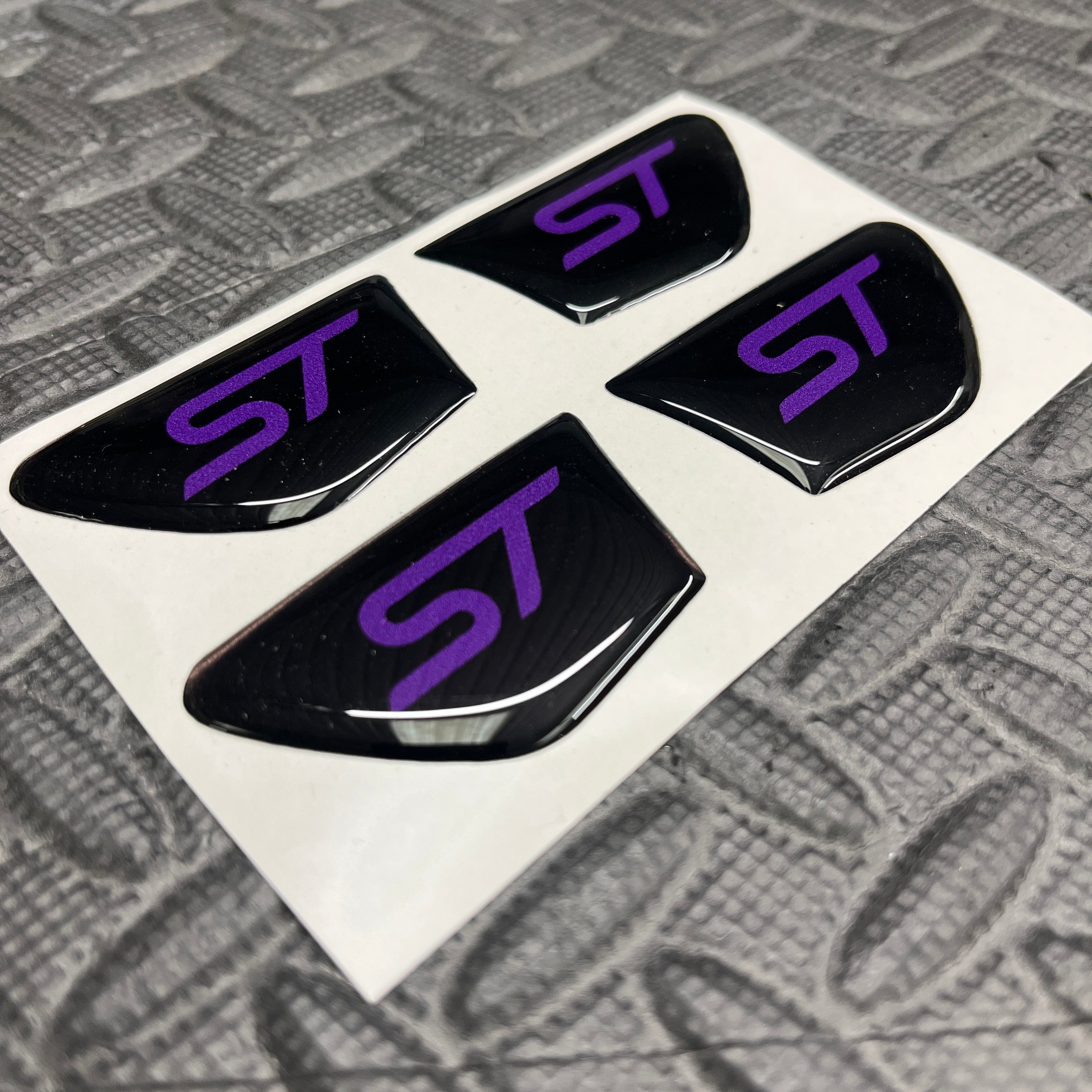Four black 'ST' logo stickers with purple lettering on a white backing.