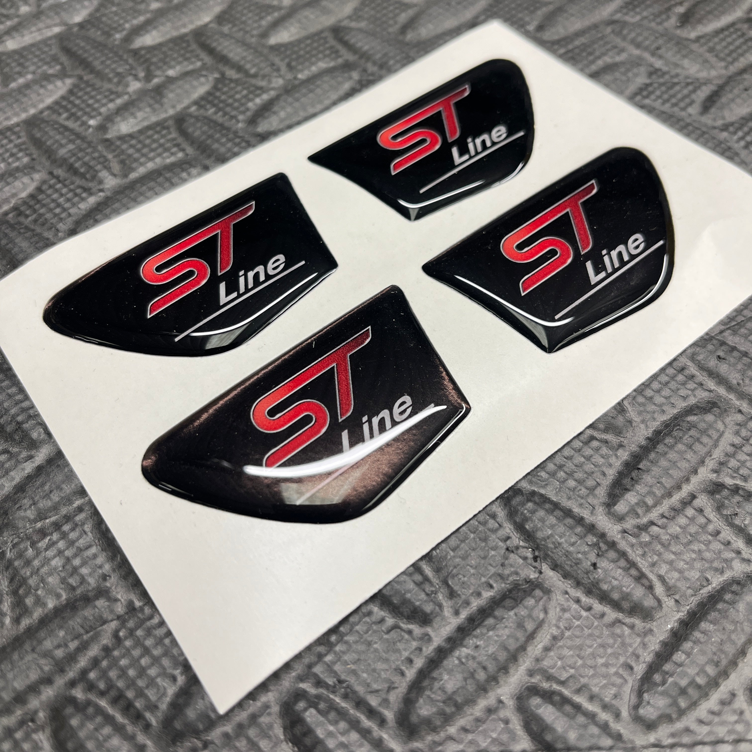 Four 'ST Line' car emblems on a white card with a textured gray background