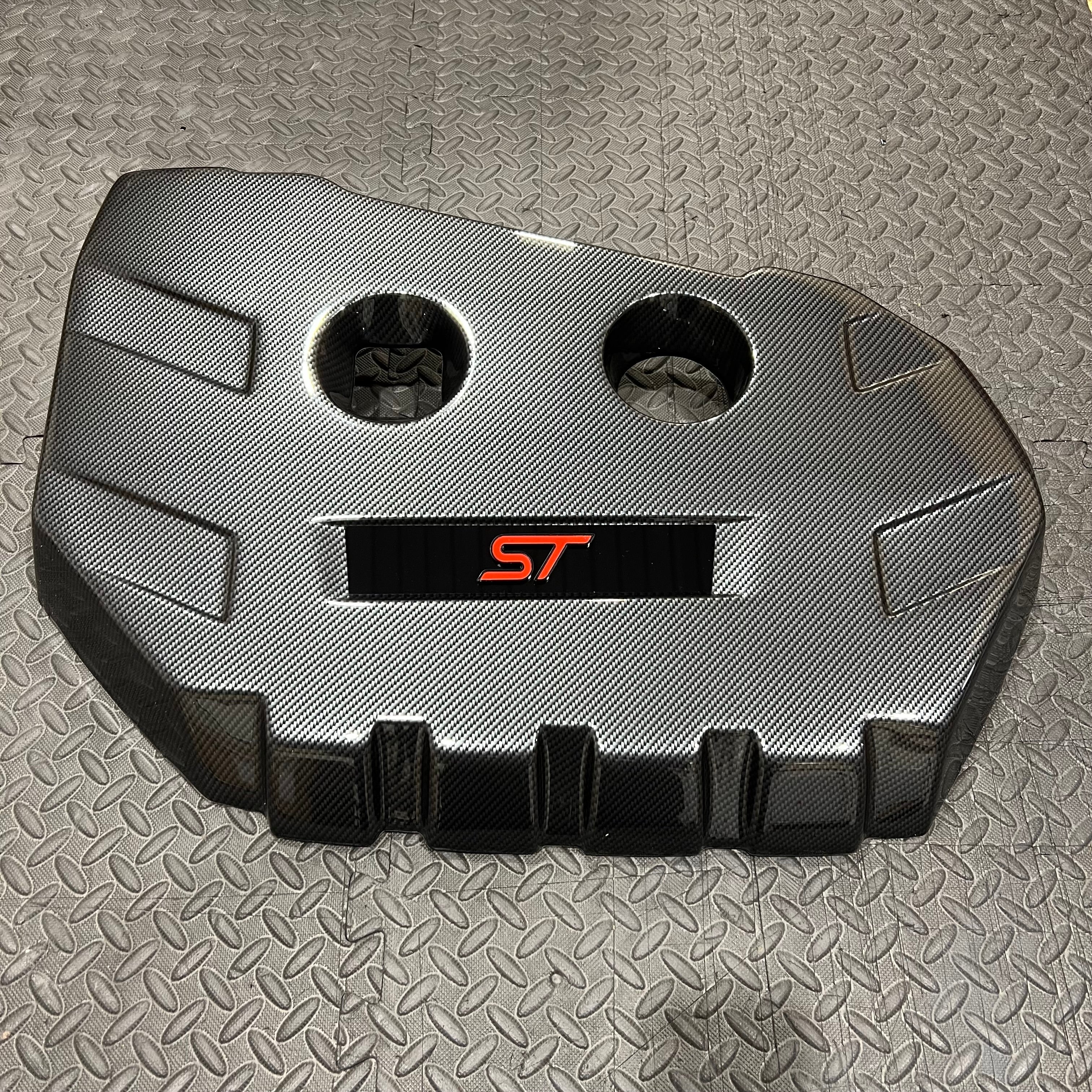 A Proform engine cover designed for a Mk3/3.5 Focus ST Petrol, featuring a carbon fibre effect plastic finish with a badge plate displaying the ST model designation.