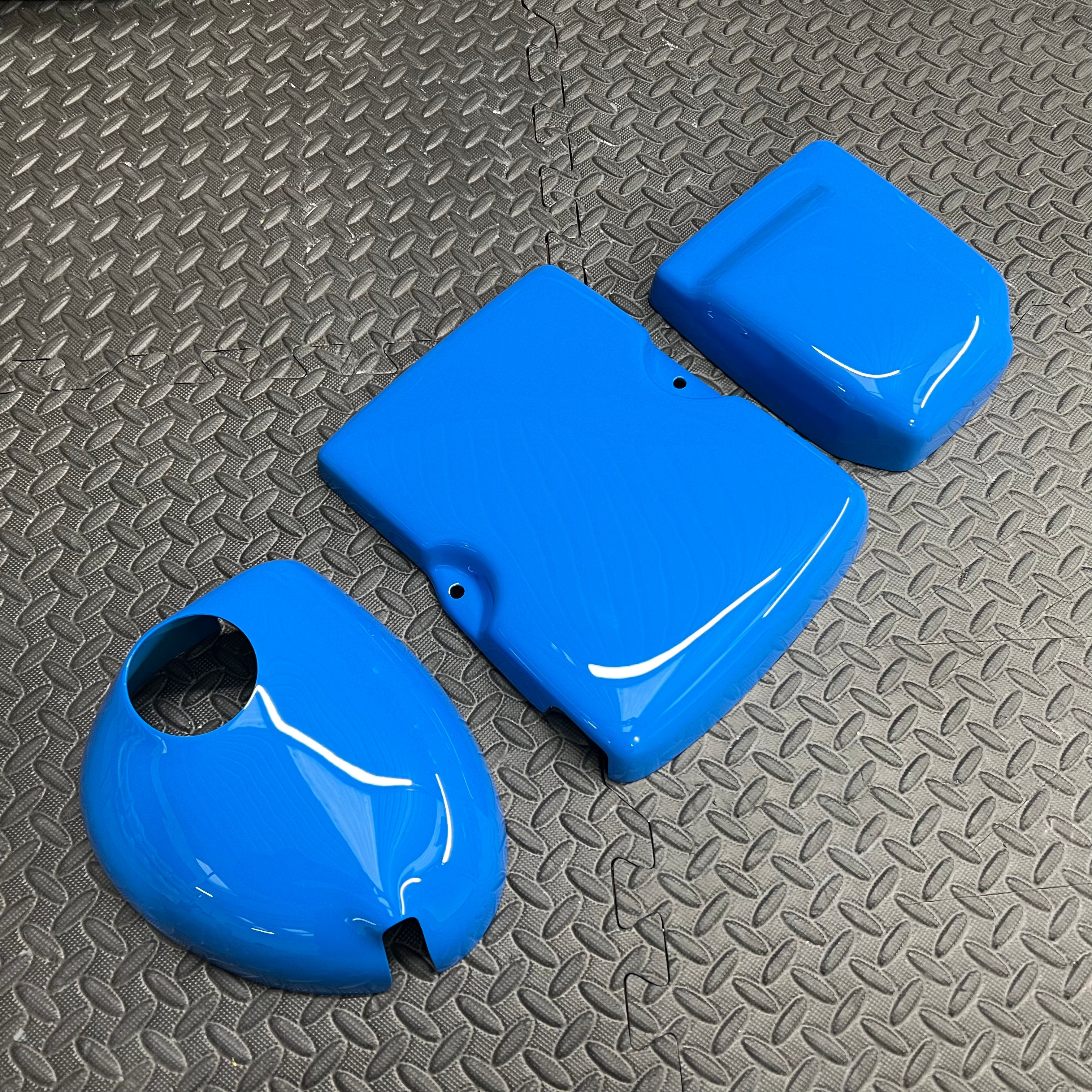 A set of blue engine bay dress up kit components including a header tank cover, battery cover, and fuse box cover.