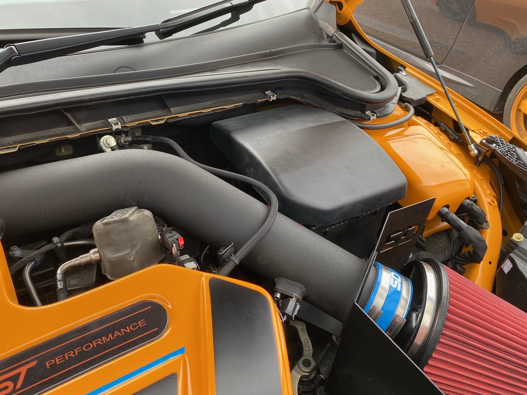 A black Proform engine bay battery cover fitted on a Ford Focus, showing the cover's placement in the vehicle's engine compartment.