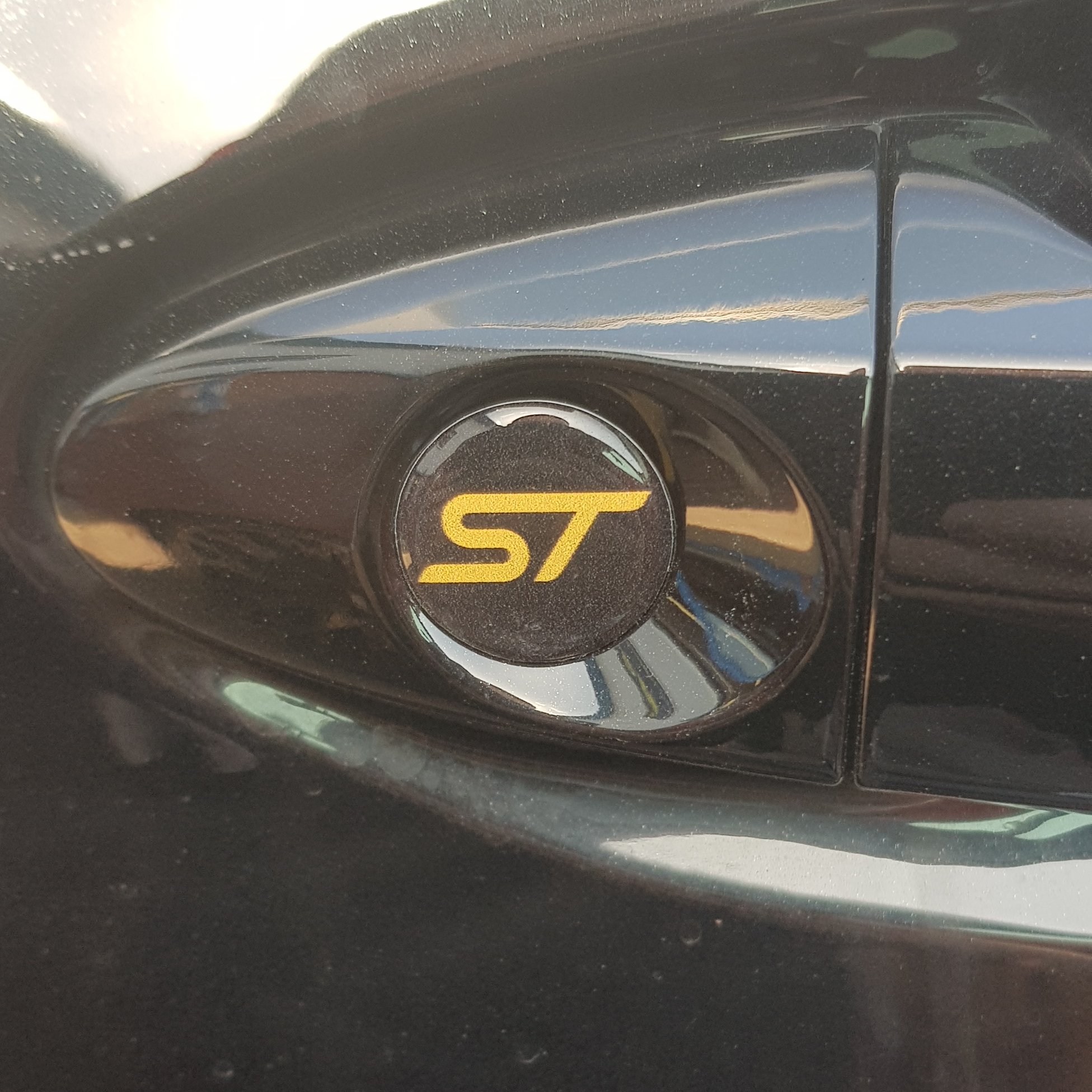 Round gel badge with the 'ST' logo applied on the exterior door lock barrel of a vehicle.