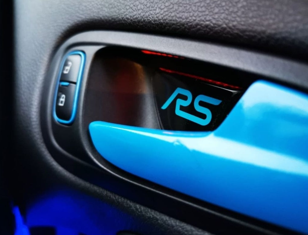 A close-up image of a custom-shaped gel badge with the 'RS' logo applied to a vehicle's interior door pull trim.
