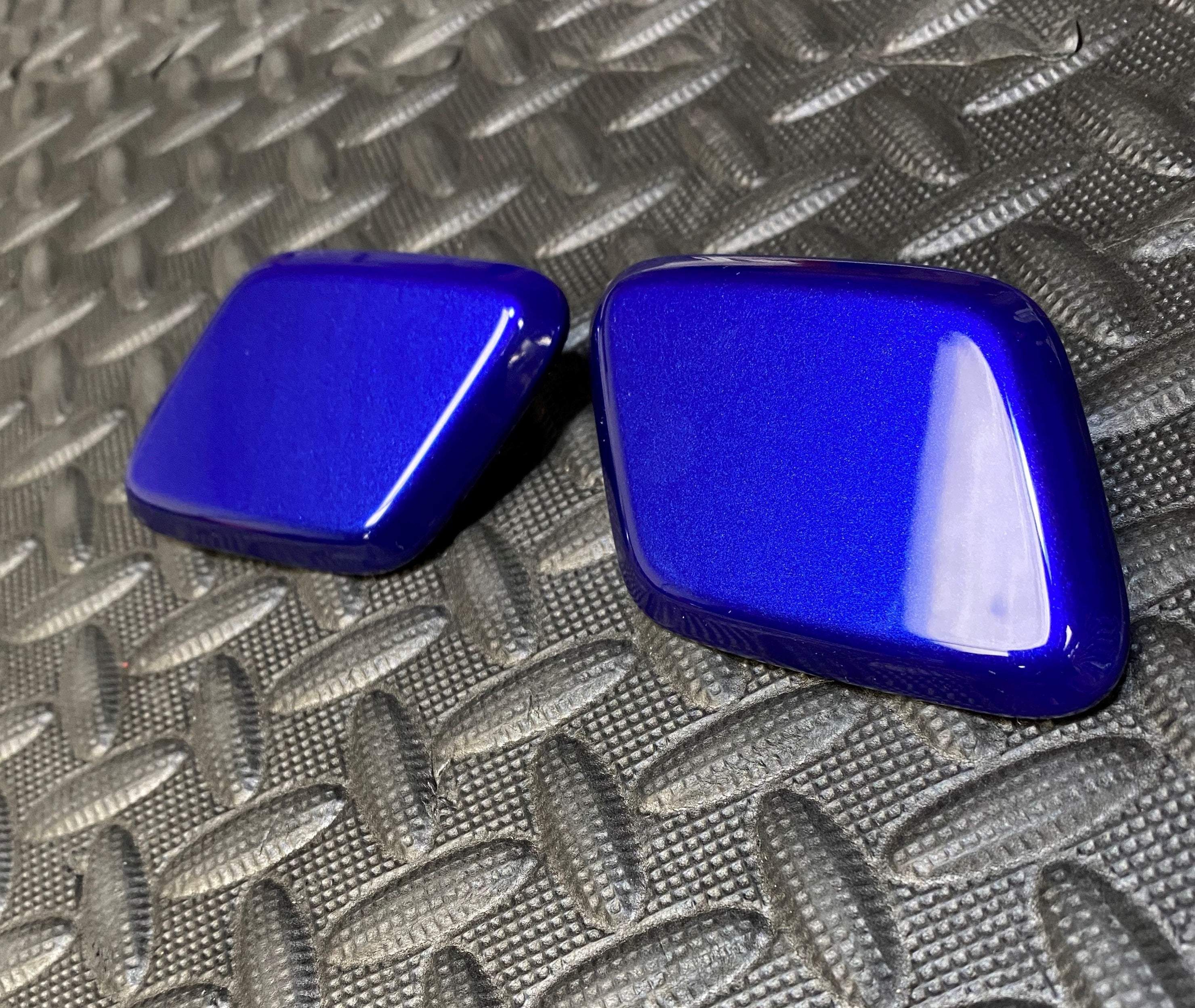 A pair of blue Ford headlight washer covers placed on a textured surface.