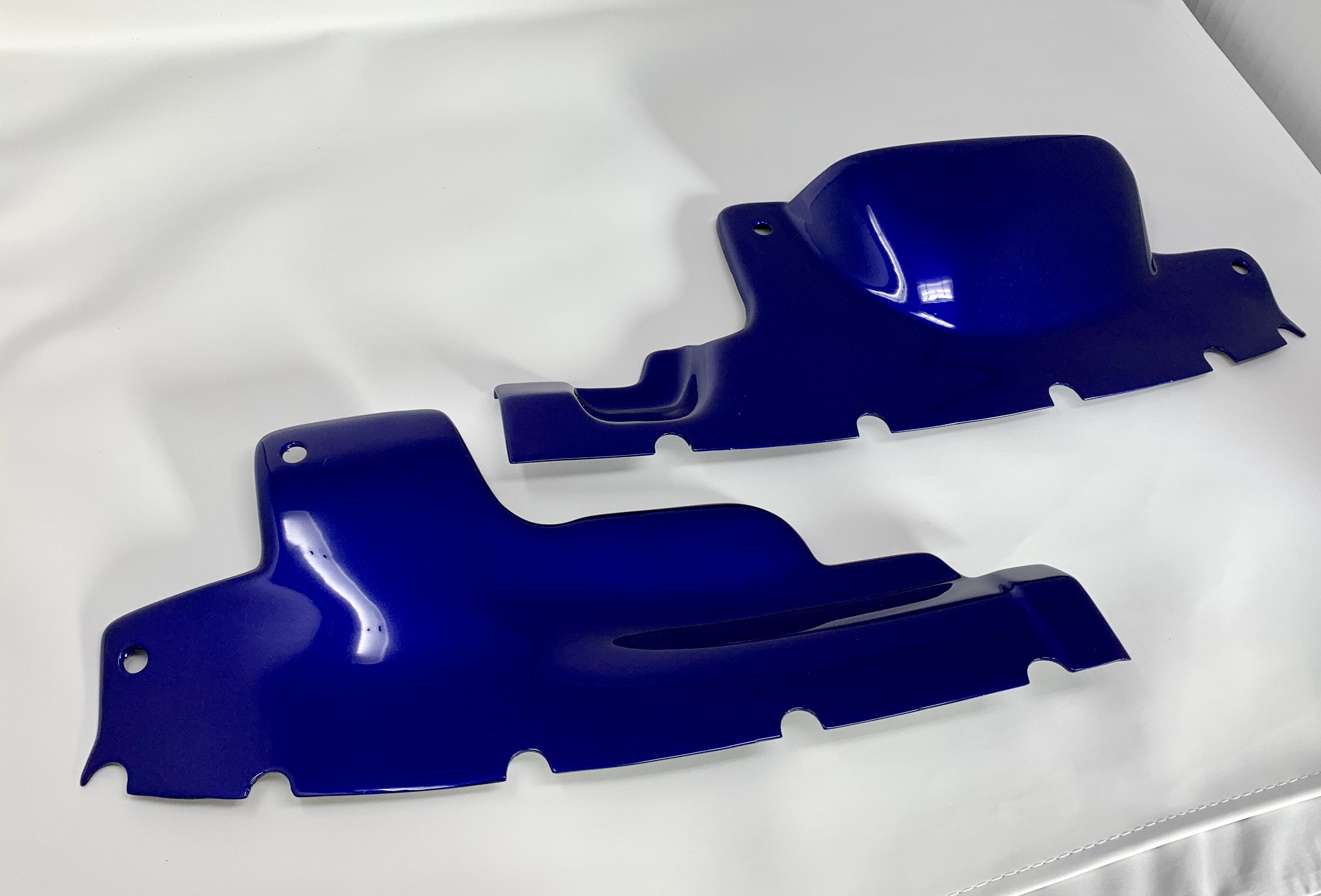 Two blue plastic engine bay slam panel covers laid on a white surface.