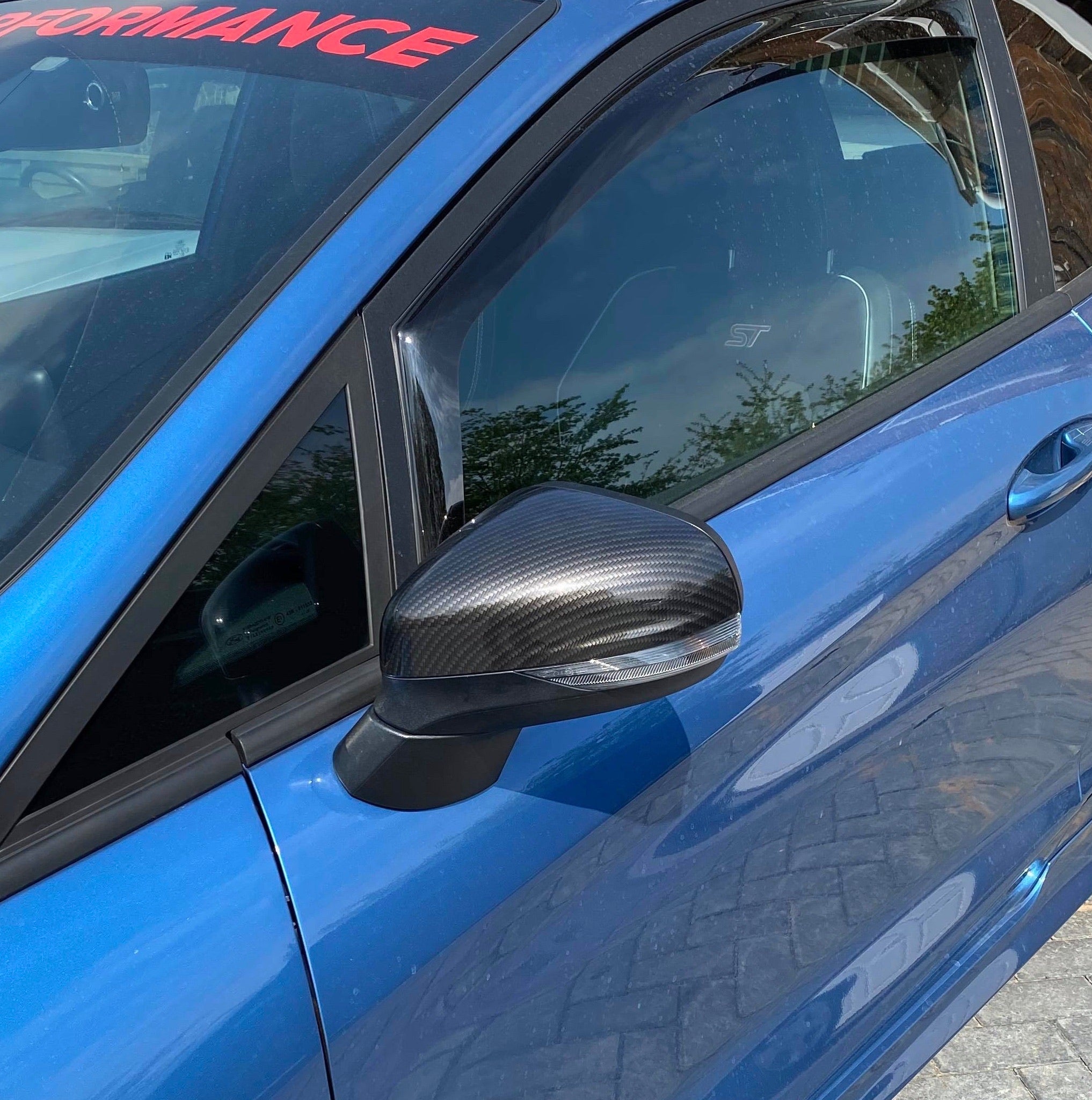 A pair of black painted mirror caps on the side mirrors of a blue Ford Fiesta Mk8.