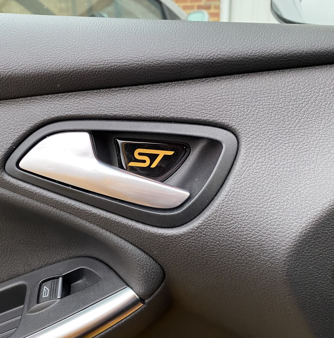 A close-up image of a custom-shaped gel badge with the 'RS' logo applied to a vehicle's interior door pull trim.