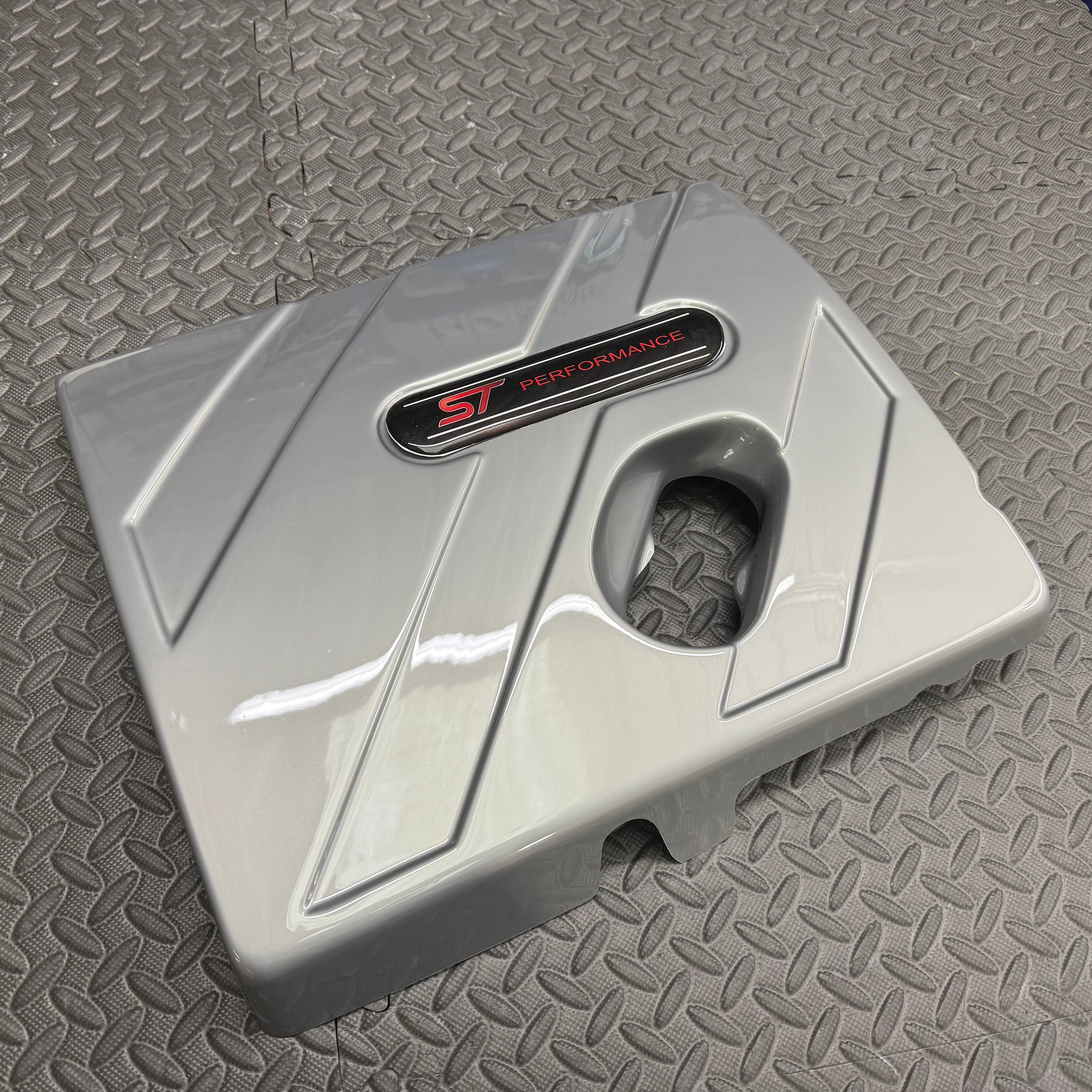 Gray metal component with 'ST Performance' logo on a textured gray surface