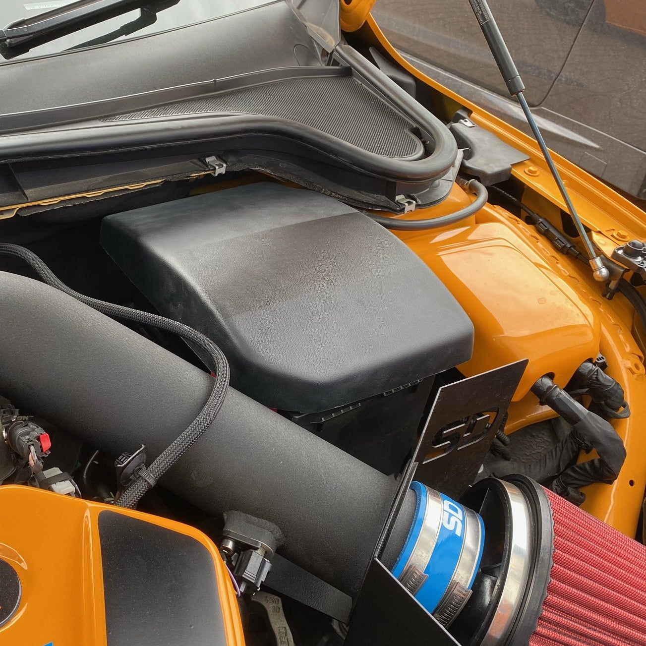 A black Proform engine bay battery cover fitted on a Ford Focus, showing the cover's placement in the vehicle's engine compartment.